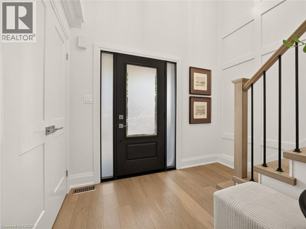 Foyer featuring wood-finish flooring, a contemporary front door with frosted sidelights, a paneled wall detail, and a staircase with a natural wood handrail and black balusters