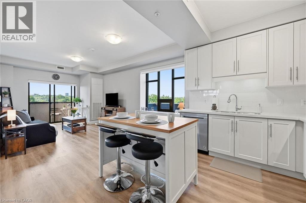 Open-concept kitchen and living area featuring wood-finish flooring, white cabinetry with stainless steel hardware, and a white subway tile backsplash