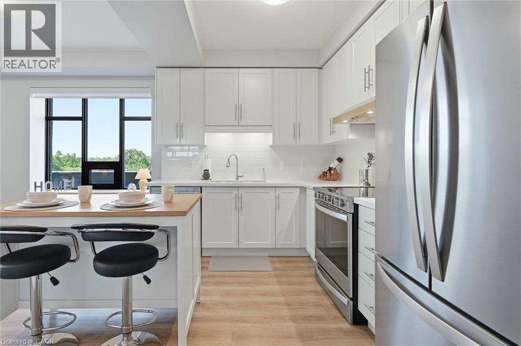Contemporary kitchen featuring white shaker cabinetry, stainless steel appliances, light wood-finish flooring, and an island with a light wood countertop