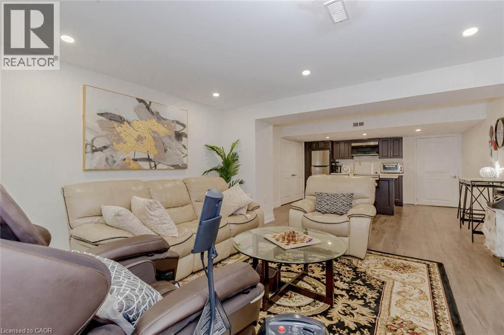 Spacious living area featuring recessed lighting, light wood-finish flooring, and a compact kitchen with dark cabinetry and stainless steel appliances