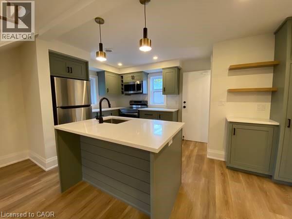 Modern kitchen featuring light wood flooring, green cabinetry, white countertops, and stainless steel appliances