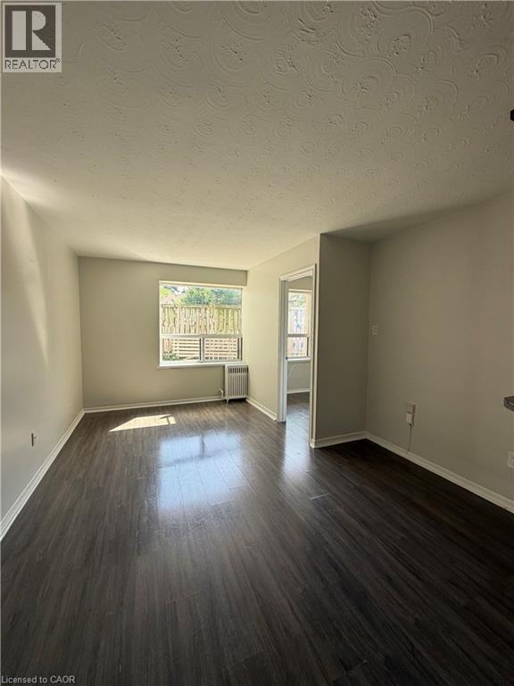 Spacious room featuring dark wood-finish flooring, light neutral-toned walls, and a textured ceiling
