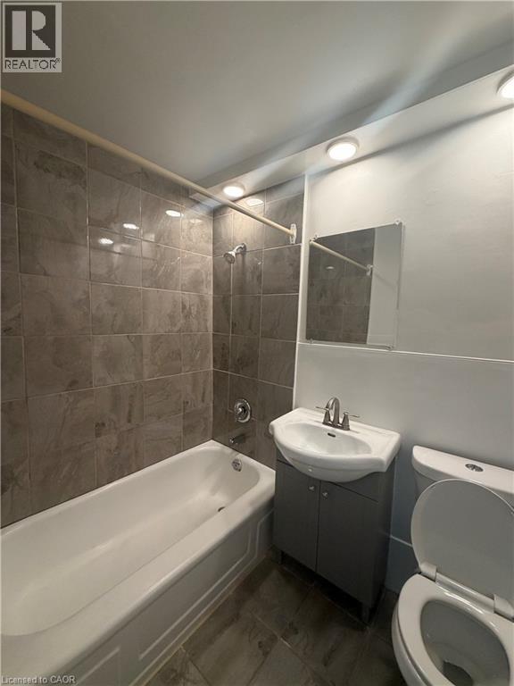 Bathroom featuring a white bathtub, floor-to-ceiling tile surround, recessed lighting, a rectangular mirror, and a vanity with a white ceramic sink