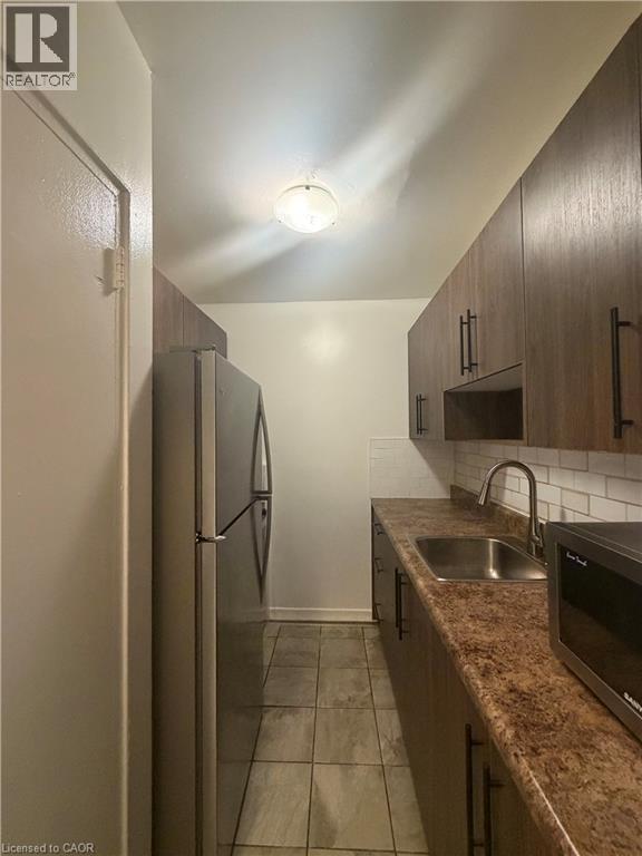 Galley kitchen featuring wood-finish cabinetry with dark hardware, a stainless steel sink, and a white subway tile backsplash