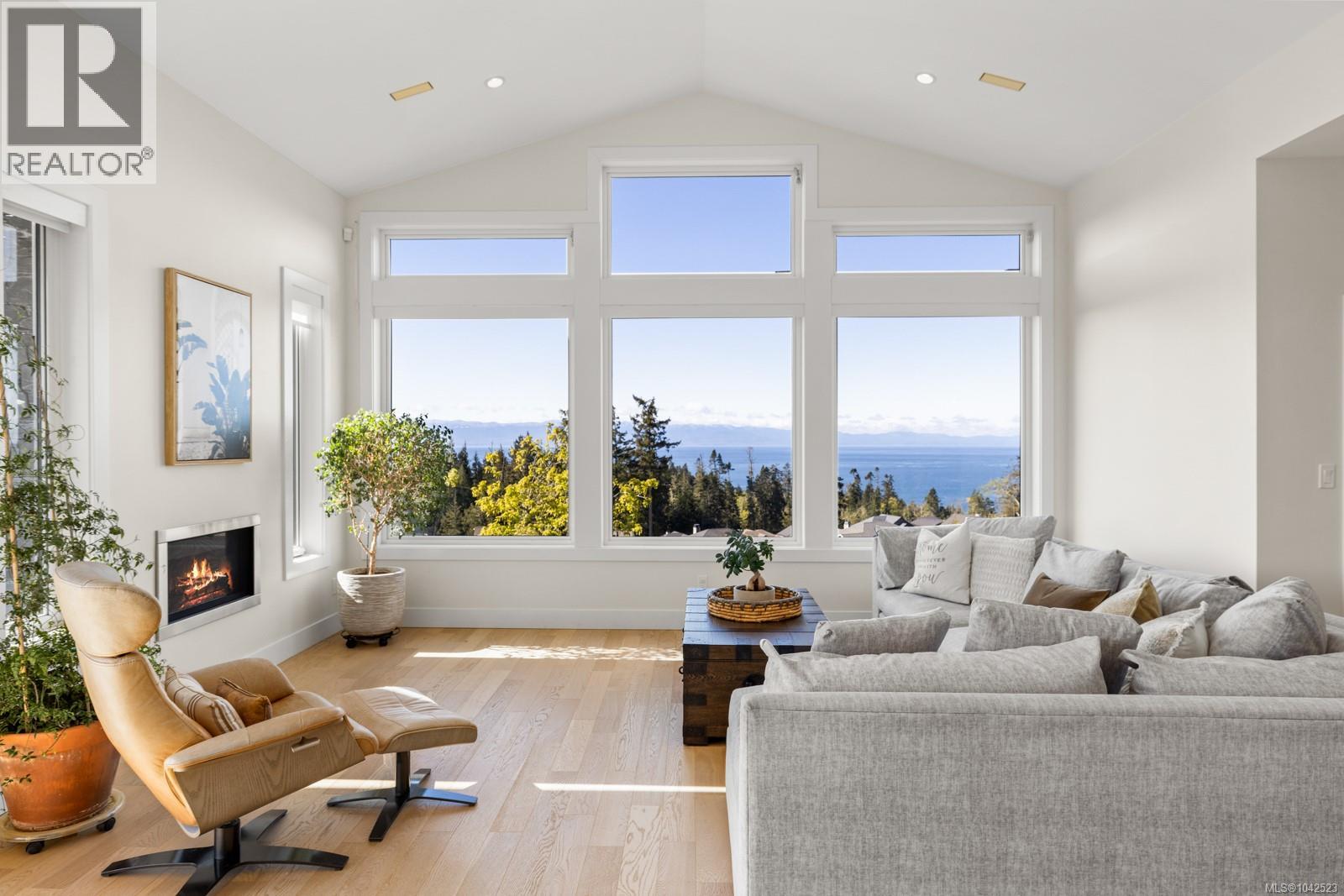 Spacious living area featuring large picture windows, vaulted ceilings, wood-finish flooring, a built-in fireplace, and recessed lighting
