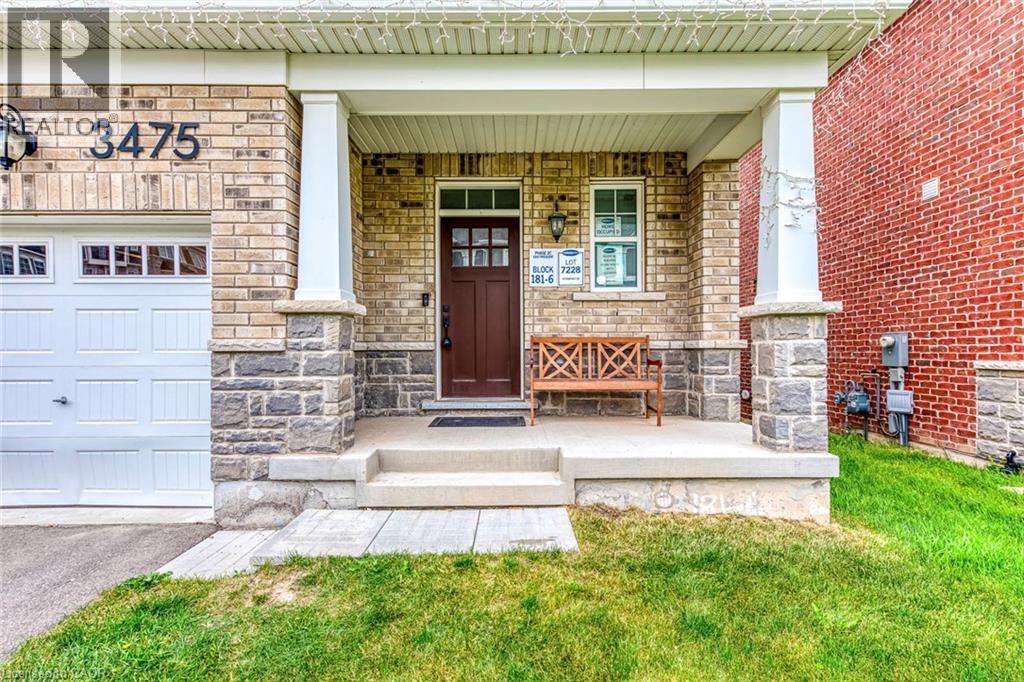Brick and stone facade featuring a covered front porch with white columns, a dark wood entry door with glass inserts, and an attached garage with a panel door and window accents