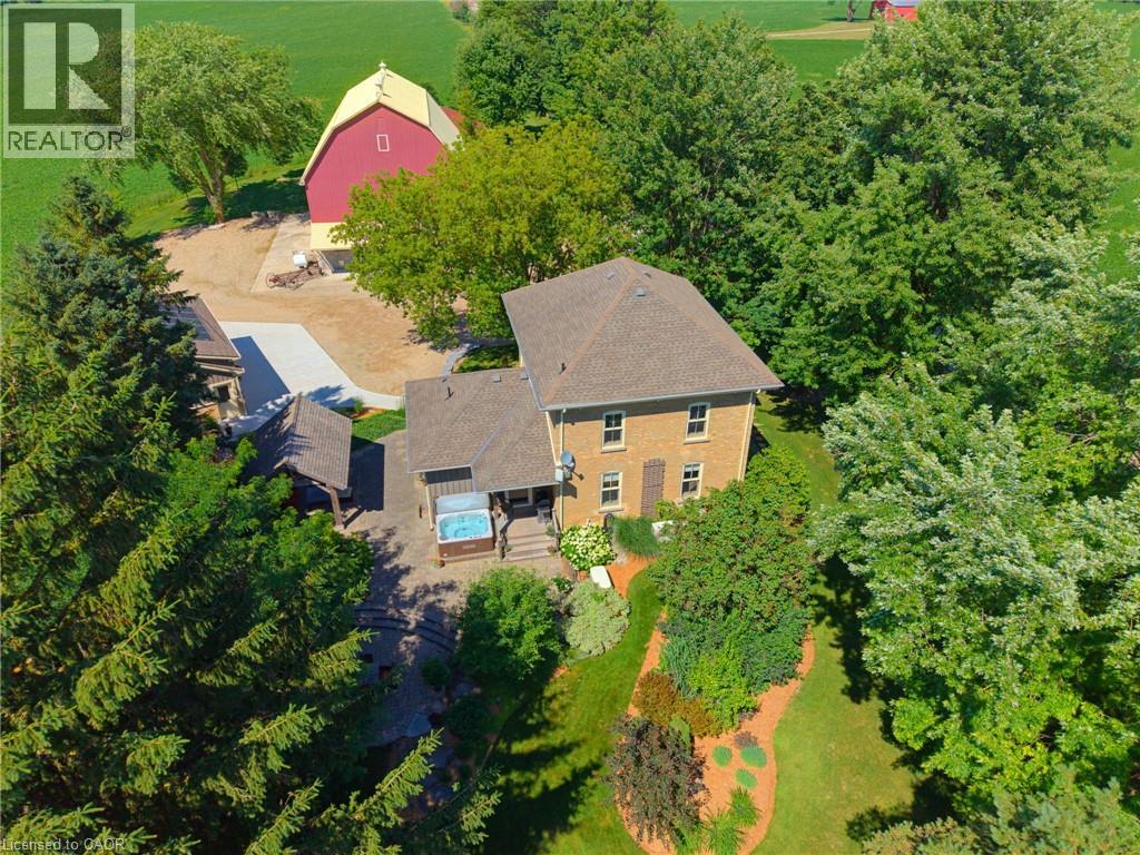 Expansive property featuring a multi-story brick residence, a red barn with a yellow roof, a covered outdoor spa, and a stone patio