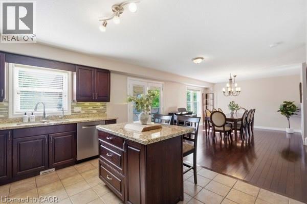Kitchen featuring dark wood cabinetry, a granite-topped island, stainless steel dishwasher, and tile flooring