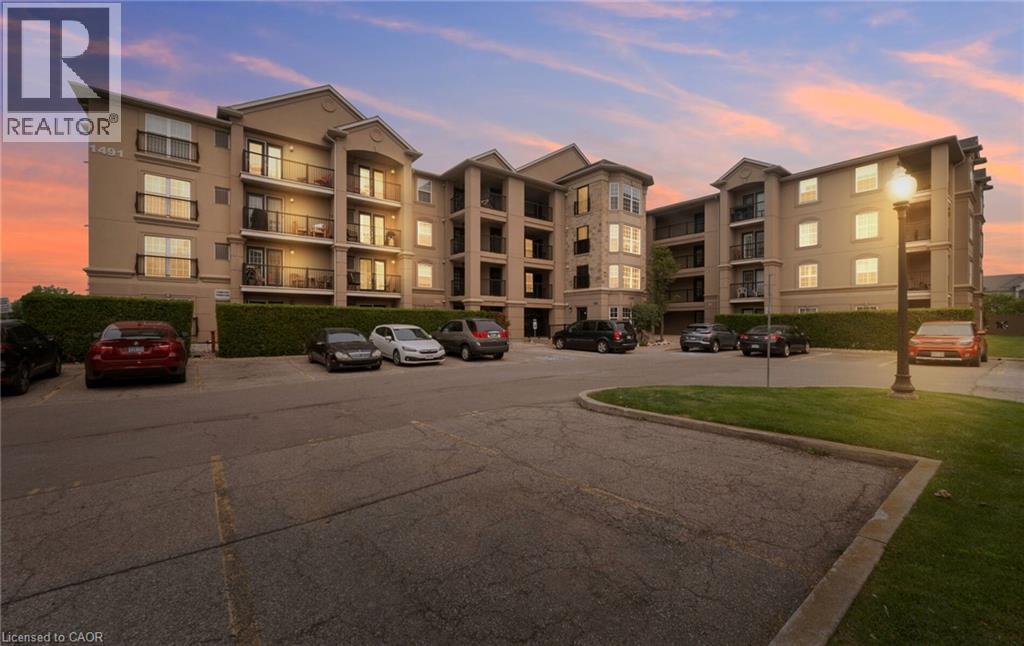 Multi-story building featuring balconies with black metal railings, bay windows, and a paved parking lot with green spaces