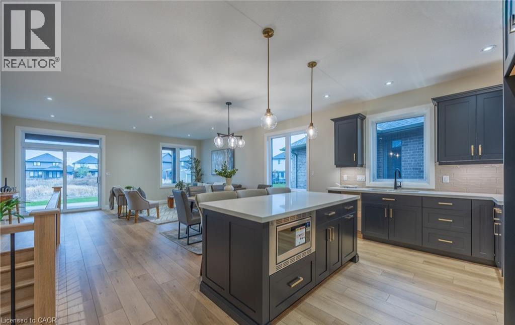 Modern kitchen featuring dark cabinetry, a central island with a built-in microwave, light countertops, and pendant lighting
