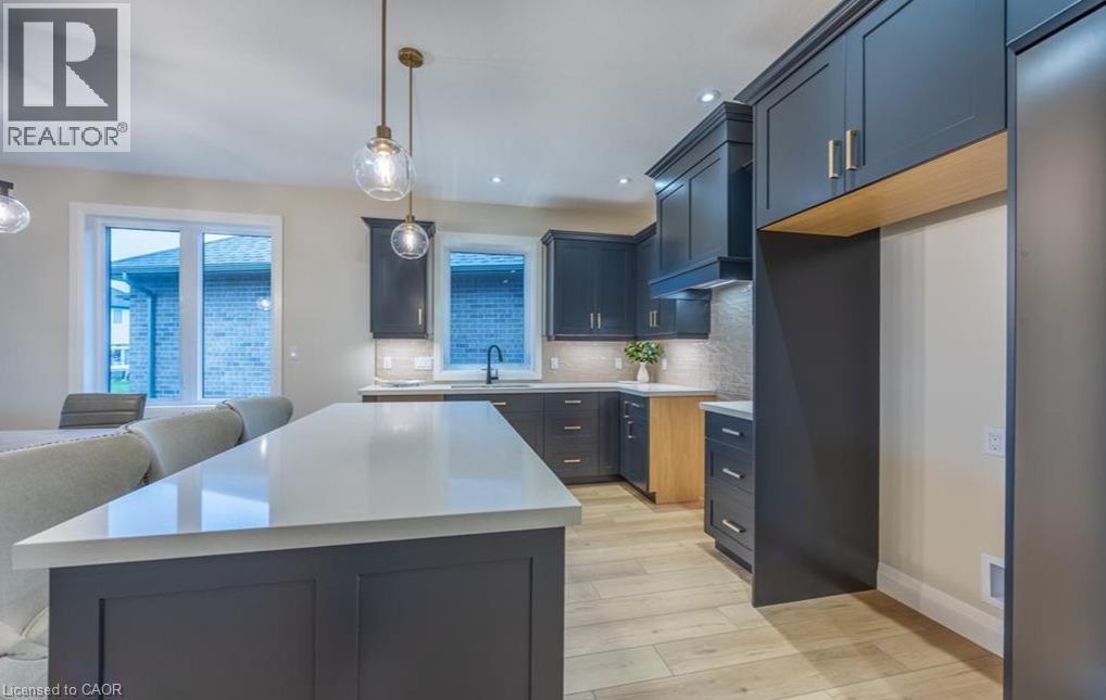 Kitchen featuring an expansive island with a light-toned countertop, dark shaker-style cabinetry, wood-finish flooring, and recessed lighting