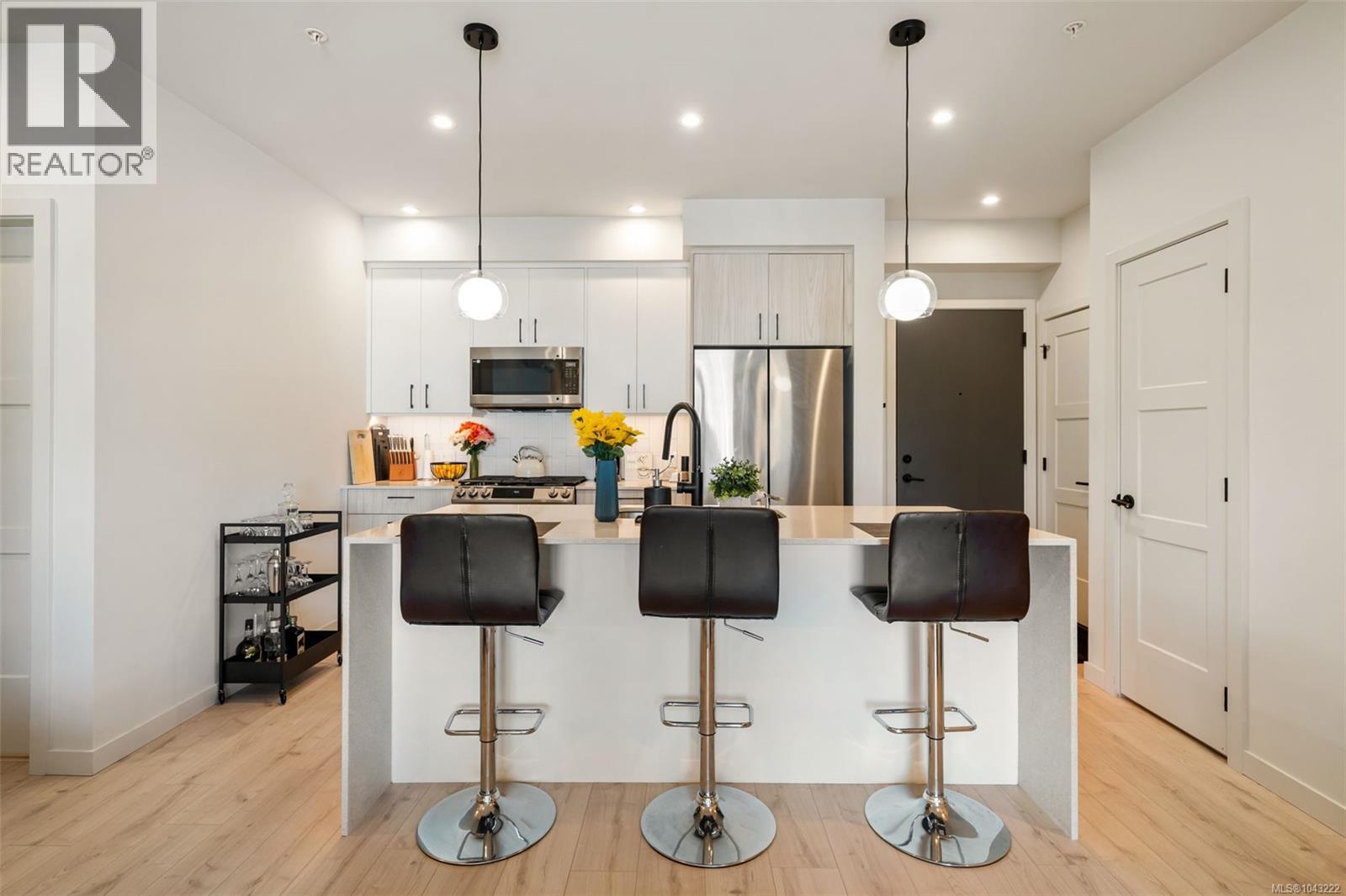Open-concept kitchen featuring an island with counter seating, stainless steel appliances, light wood-finish flooring, and pendant lighting
