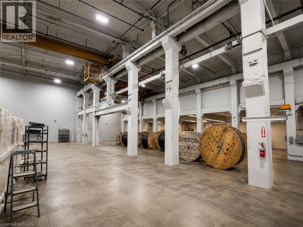 Spacious industrial interior featuring concrete flooring, tall ceilings, exposed structural beams, a large overhead crane system, and wall-mounted fire extinguishers