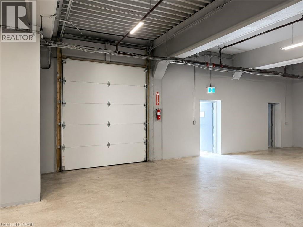 Spacious interior featuring a large white overhead door, exposed industrial-style ceiling, polished concrete flooring, recessed lighting, and a separate entrance