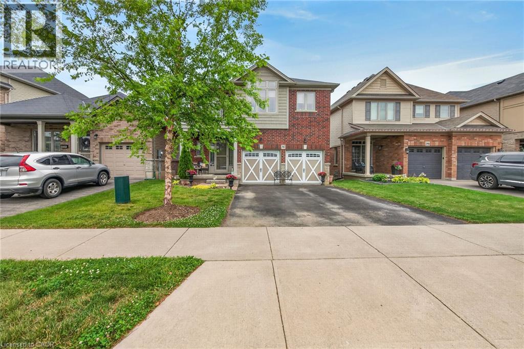 Charming brick exterior with double garage doors and manicured front lawn anchored by a mature shade tree