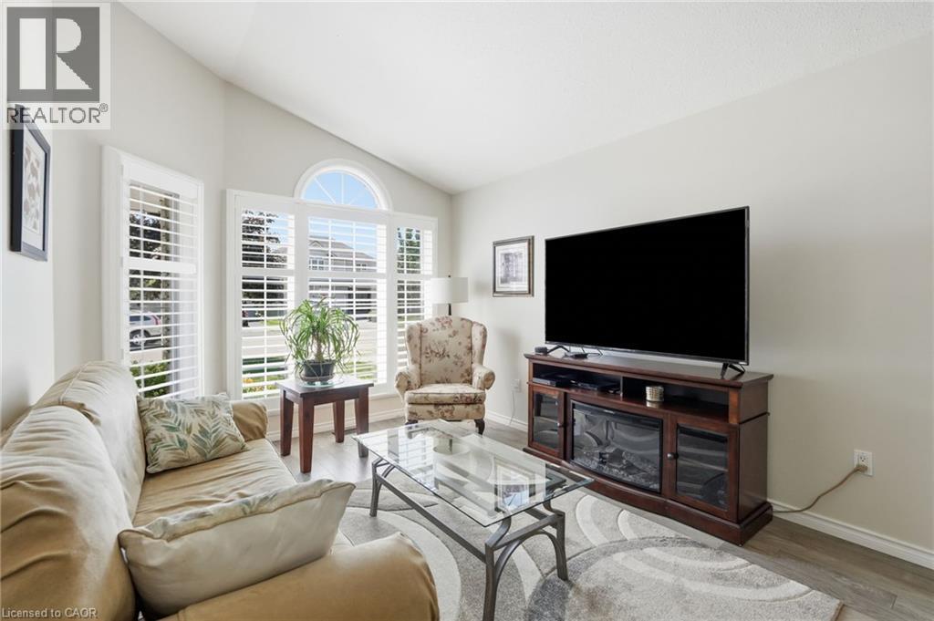 Living area featuring a vaulted ceiling, multiple windows with white plantation shutters, a half-round transom window, and wood-finish flooring