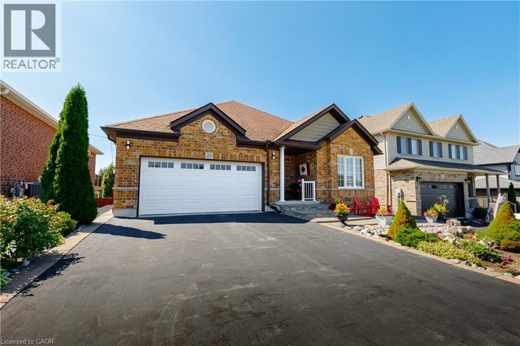 Brick Colonial home featuring a two-car attached garage with white panel doors, circular window detail above the entry, and manicured landscaping with mature evergreen plantings and seasonal flower be