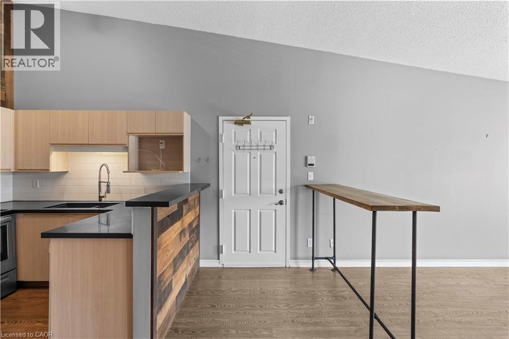 Kitchen featuring light wood-finish cabinetry, black countertops, and a white subway tile backsplash