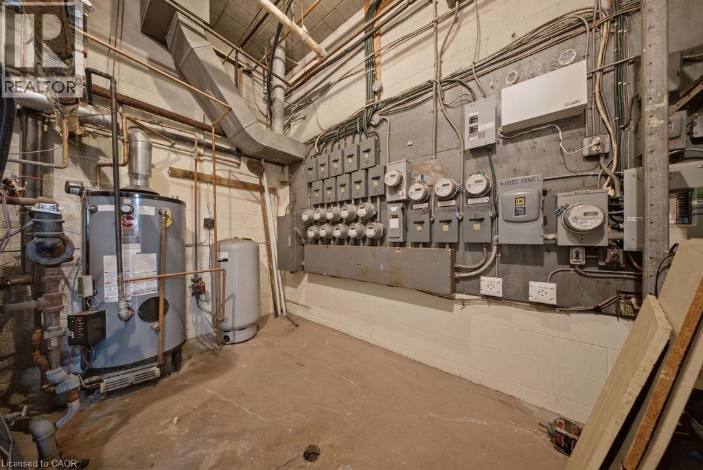 Utility room featuring exposed copper piping, a large hot water heater, expansion tank, multiple electrical meters, and concrete flooring