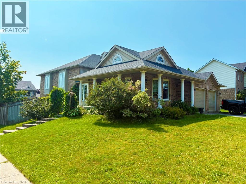 Brick Colonial home featuring a covered front portico with tapered columns, arched gable dormers with circular windows, and a professionally landscaped front yard with mature shrubs and a manicured la