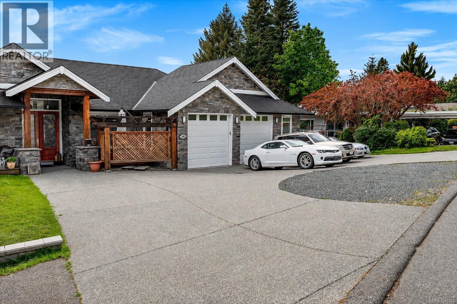 Stone veneer exterior with wood beam accents, two-car garage, red entry door with glass paneling, and a large paved driveway