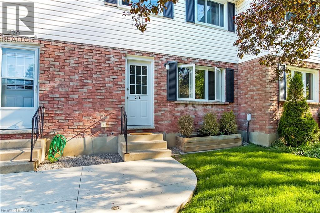 Brick and siding exterior featuring multiple entry doors, a curved concrete walkway, and established landscaping with a wooden planter box