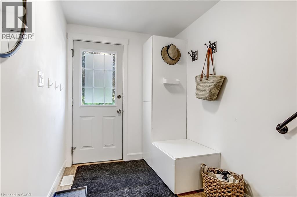 Entryway featuring a white door with frosted glass panels, wood-finish flooring, a built-in white bench, a built-in wall panel with a shelf, and wall-mounted coat hooks
