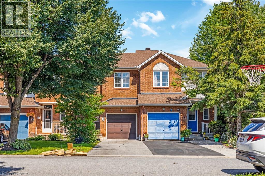 Brick facade townhome with individual garage, covered front porch, and mature trees