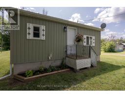 Exterior of house with green siding, white door, decorative railings, and shutters - 2956 County Road 14 Stone Mills