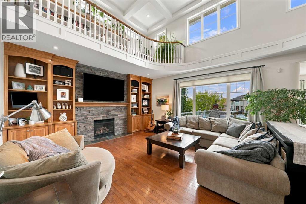The stunning living room features a two-storey high coffered ceiling and a gas fireplace with stone surround, custom cabinetry, and shelving