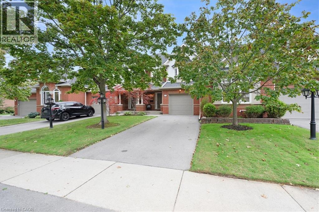 Red brick exterior with white trim, attached garage, paved driveway, mature trees, and street lamps