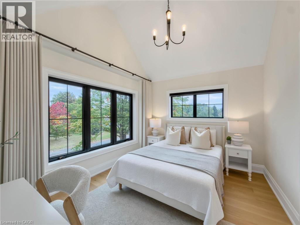 Vaulted ceiling with a black metal chandelier, oversized black-framed windows, wood-finish flooring, and light-toned walls