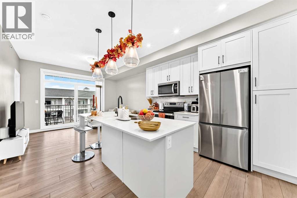 Open kitchen featuring white cabinetry, stainless steel appliances, a large island with seating, and modern pendant lighting