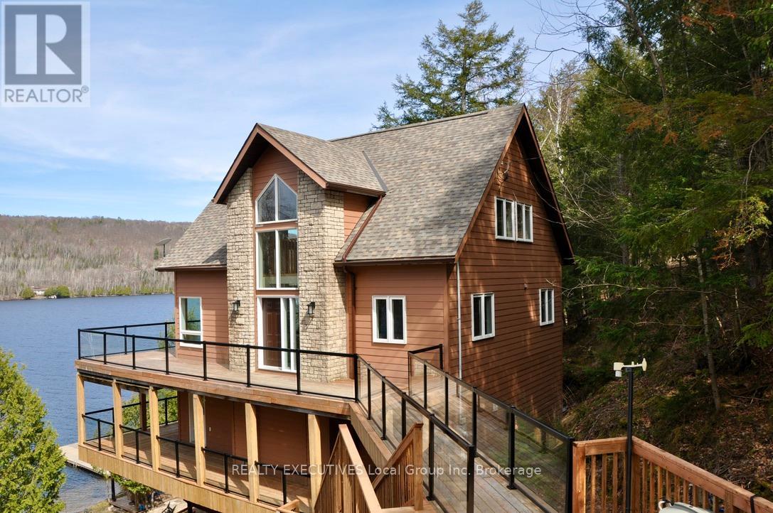 Discover exceptional year round waterfront living on the pristine shores of Trout Lake. This beautifully crafted Viceroy home, built in 2005, offers 148 feet of sandy shoreline, crystal-clear water, and unmatched privacy. Enjoy breathtaking lake views from every angle of this custom-designed property.The open-concept main floor features soaring vaulted ceilings and expansive windows that flood the space with natural light. Two generously sized bedrooms are located on the main level, while the loft-style primary suite has a walkway that overlooks the great room, creating a spacious and airy ambiance. Two bathrooms and the kitchen have heated floors. The lower level includes a large family room, a separate entrance, a fourth bedroom and its own covered deck perfect for guests or extended family. Step outside to enjoy the lakeside sauna, pavilion, and a substantial dock system that can accommodate a 24' boat.  The sand beach is ideal for kids with shallow water by the shore but with diving opportunities off the dock. Trout lake is wonderful for swimming, fishing and boating in the summer but equally exciting in the winter with access to world class snowmobile trails, right from your driveway.  A rare opportunity to own a turnkey lakeside getaway with both elegance and functionality. (id:48254)