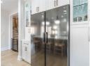 Kitchen view of freestanding refrigerator, light wood finished floors, white cabinetry, glass insert cabinets, and light countertops