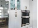 Kitchen with freestanding refrigerator, stainless steel double oven, white cabinets, and glass insert cabinets