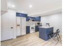 Kitchen with blue cabinets, white appliances, light countertops, light wood-style flooring, and recessed lighting