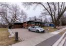 Single story home with a chimney, driveway, an attached garage, and brick siding