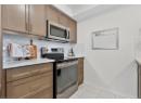 Kitchen with stainless steel appliances, backsplash, light tile patterned floors, light stone counters, and brown cabinets