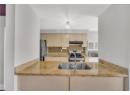 Kitchen with appliances with stainless steel finishes, backsplash, light stone counters, under cabinet range hood, and a chandelier