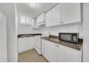 Kitchen with white electric stove, white cabinets, black microwave, under cabinet range hood, and light tile patterned flooring