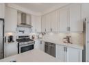 Kitchen with appliances with stainless steel finishes, white cabinetry, wall chimney range hood, light stone countertops, and backsplash