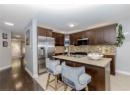 Kitchen with dark brown cabinetry, appliances with stainless steel finishes, decorative backsplash, a center island with sink, and glass insert cabinets