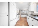 Kitchen featuring white appliances, light wood finished floors, dark countertops, and white cabinetry