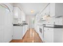 Kitchen with white appliances, under cabinet range hood, dark countertops, tasteful backsplash, and light wood-style floors