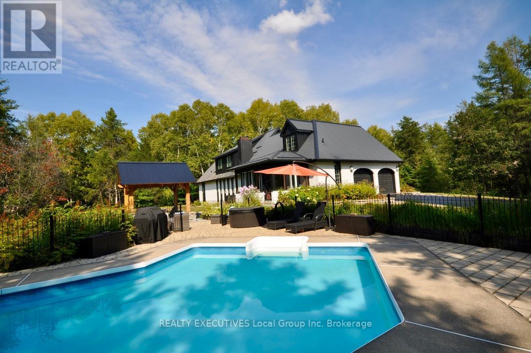 Welcome to this one-of-a-kind, 5-acre estate lot located within the city limits of North Bay, offering exceptional privacy, space, and lifestyle amenities. Nestled among mature trees and set well back from the road, this property is accessed via two paved driveways and offers a rare blend of seclusion and convenience.  Step into the home through the bright sunroom overlooking the backyard pool area, and instantly feel the welcoming charm. The eat-in kitchen is well appointed, featuring cherry cabinetry, a brick fireplace, and warm country finishes. The living room is flooded with natural light from large windows and made cozy by a pellet stove, while the dining room is tastefully finished and looks out over the serene, private yard.  The main-floor primary bedroom offers a quiet retreat with a 4-piece ensuite bath and its own sunroom, ideal for peaceful morning coffee or evening relaxation. Upstairs, you'll find two generously sized bedrooms, both with walk-in closets, a full 4-piece bathroom, and a separate wing with a flex room that can serve as a fifth bedroom, office, or studio. The lower level is designed for entertaining, featuring a live edge bar, a wine room, and a cozy rec room with a wood-burning fireplace. This level also includes a fourth bedroom, a 3-piece bath, and a cedar-lined sauna, adding a touch of luxury to everyday living.  Step outside into your private summer oasis, complete with an in-ground pool, a gazebo, and a custom fire pit area, perfect for hosting or simply enjoying quiet evenings under the stars.  Attached 2 car garage.  Rounding out the property is a detached 40 x 40 garage with multiple overhead doors, ideal for a workshop, storage, or recreational use. A 20 x 20 bonus room within the garage adds even more flexible space for a studio, gym, or guest suite.Whether you're a family looking for room to grow, an outdoor enthusiast, or someone seeking a private retreat with city amenities, this incredible property has it all. (id:48254)
