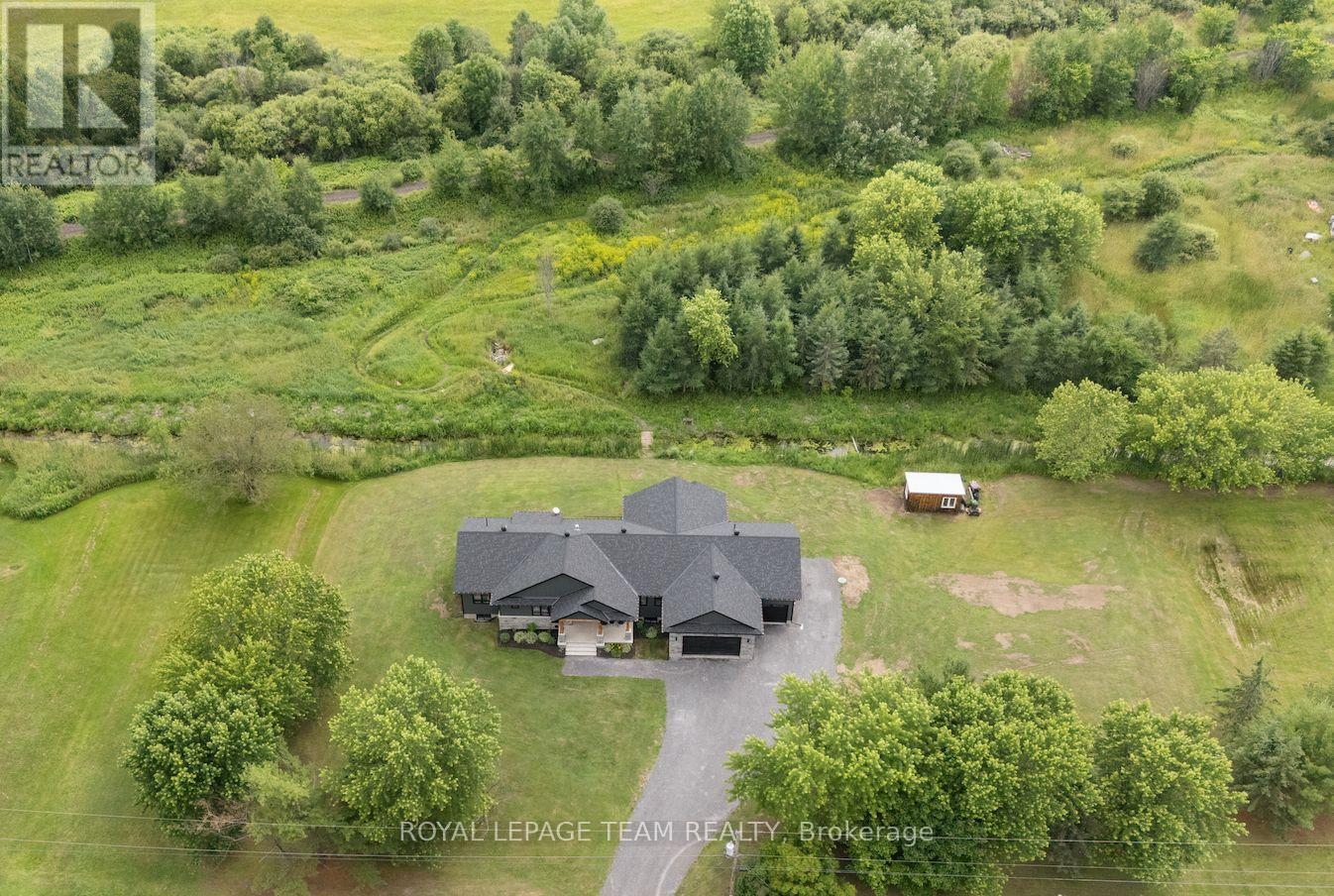 IN-LAW POTENTIAL! 2+ ACRES! NO REAR NEIGHBOURS! HEATED OVERSIZED TRIPLE CAR GARAGE! Where modern design meets natural beauty-this is country living, reimagined. This custom bungalow showcases a striking, moody exterior-a rich blend of dark board & batten, stone & timber that quietly pays tribute to its surroundings. Deer pass the treeline & a gentle stream winds through the property. Step inside & the home immediately opens up-9' & 10' ceilings, 8' doors & wide-plank flooring creating a space that feels both expansive & grounded. At the centre, a beautifully designed kitchen balances style & function w/ quartz counters, an oversized island, side bar & a rarely offered butler's pantry room. From here, the home naturally gathers-anchored by a fireplace framed w/ floating shelves & a 10' tray ceiling overhead, while sunlight pulls you toward the rear deck & enclosed porch, extending everyday living outdoors. Tucked just off this space, a glass-accented den offers flexibility. Privately set, the primary suite is capped by a 10' tray ceiling, 2 walk-in closets & a refined ensuite. 2 additional bedrooms are positioned at the front, sharing a beautifully finished full bath. Everyday function is elevated through a well-planned back hall w/ mudroom, powder room & a pinterest worthy laundry space w/ cabinetry, quartz & sink. Downstairs, the groundwork is already in place-large windows, bath & wet bar rough-ins, partial framing & direct garage access create strong in-law or income potential. And for those who need more-an oversized heated garage w/ extended height, double door & a 3rd drive-thru bay (front & rear access) delivers unmatched versatility. All just minutes to Stonecrest PS, West Carleton SS, Constance Bay & Kanata amenities. A lifestyle, not just a home. (id:48254)