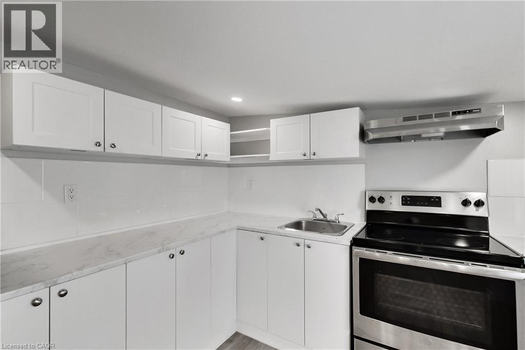 Contemporary kitchen featuring white cabinetry, light-toned countertops, a stainless steel range, and a coordinating range hood
