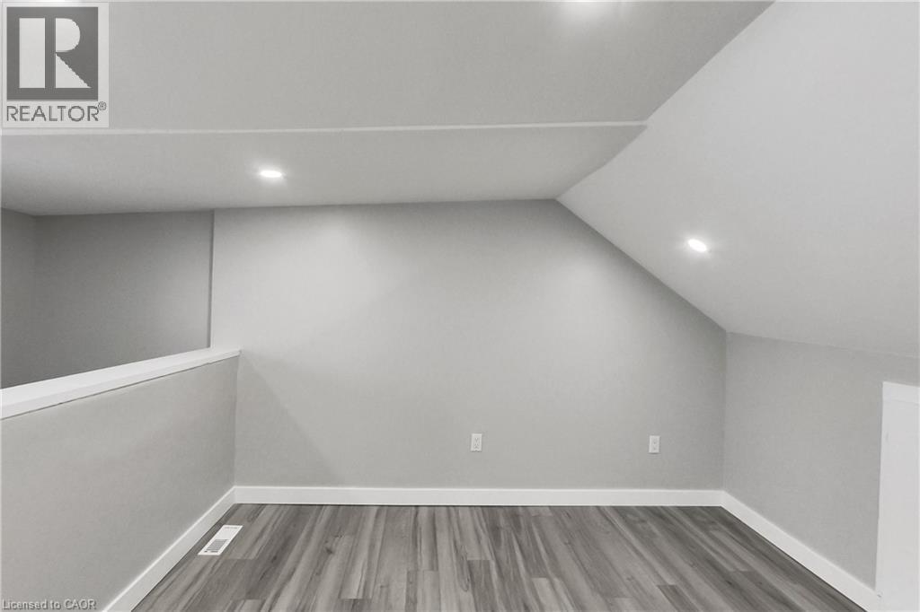 Sloped ceiling with recessed lighting, wood-finish flooring, and a low wall partition