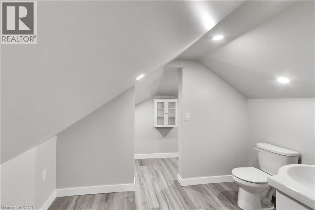 Sloped ceilings with recessed lighting, wood-finish flooring, built-in wall cabinet with glass-front doors, toilet, and sink